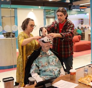 senior man trying on VR headset with help of Senior Planet staff